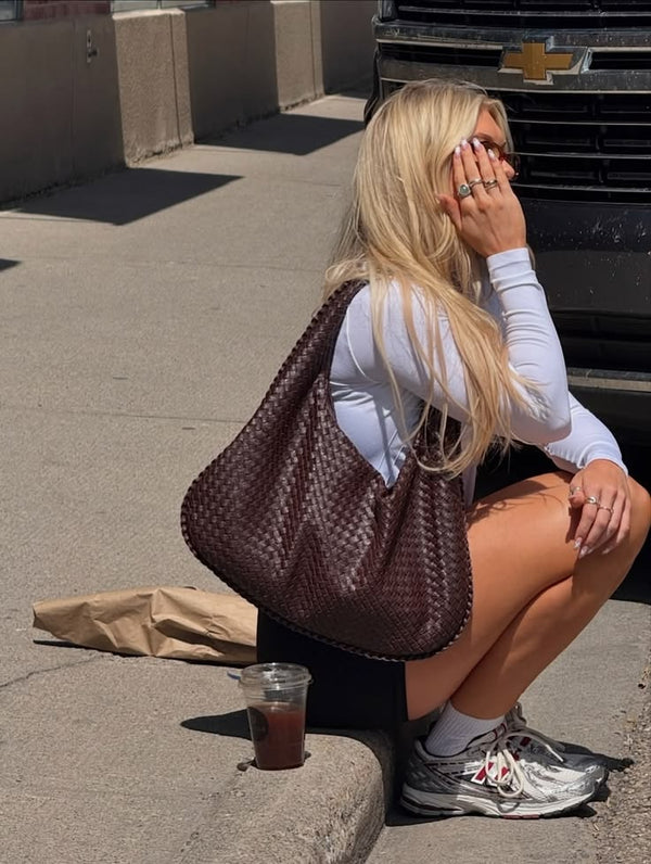 seated woman carrying dark brown woven shoulder bag