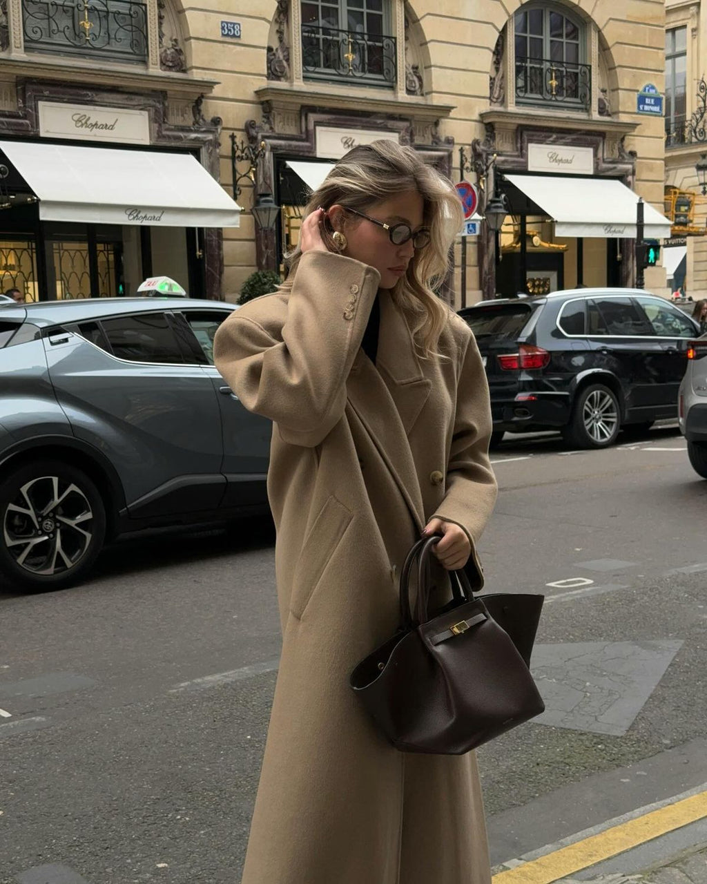 Woman in a camel coat carrying the brown Manhattan Tote on a city street