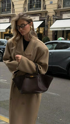 Woman carrying the brown Manhattan Tote by its top handles with a camel coat