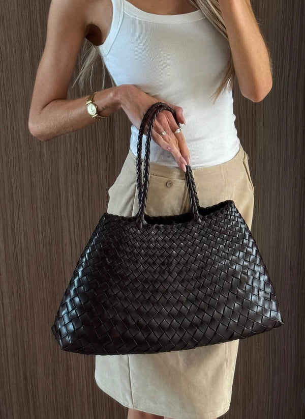 woman holding black woven tote bag with white outfit