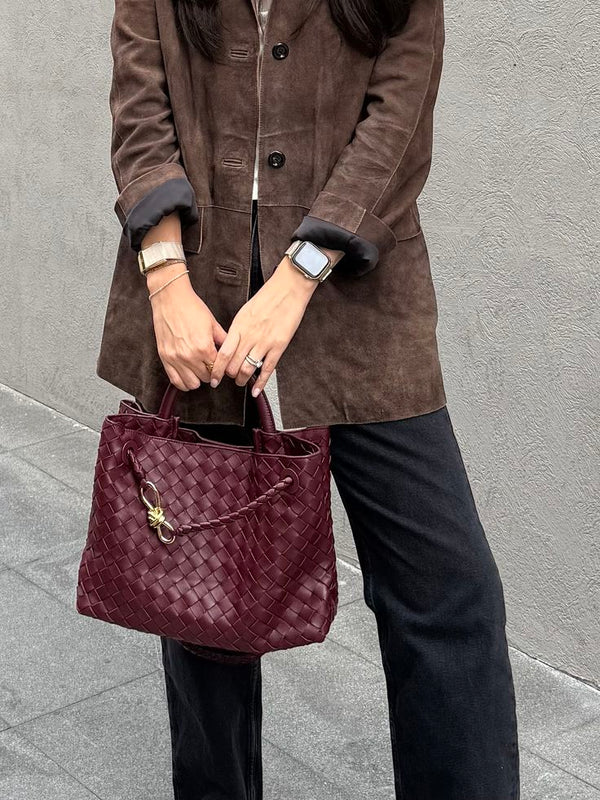 person in brown coat holding burgundy woven tote bag