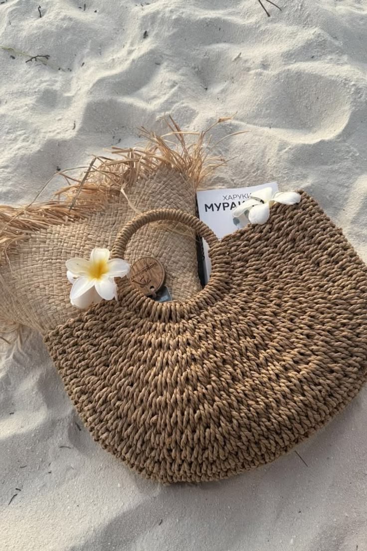brown crescent straw bag flat lay on sand with summer accessories