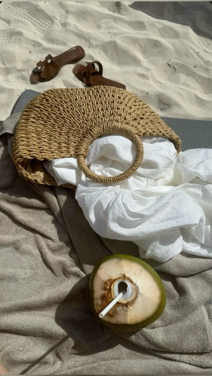 brown crescent straw bag beach flat lay with coconut and white dress
