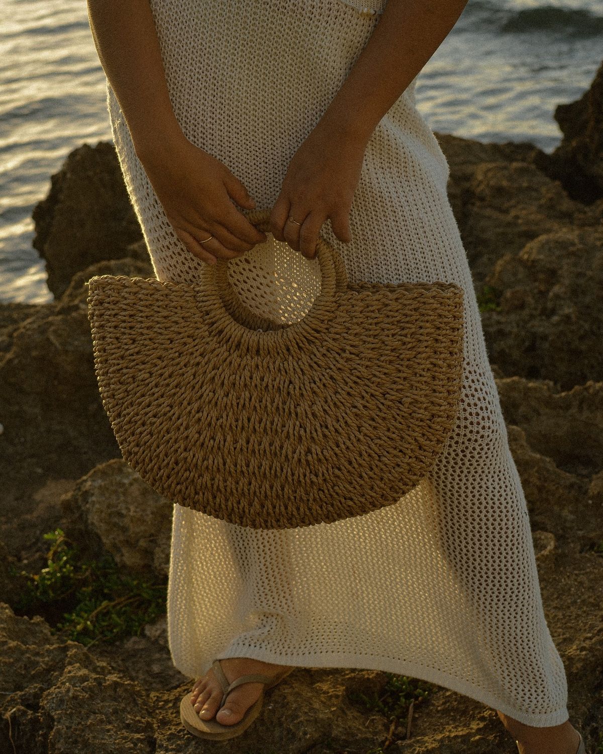 woman holding brown crescent straw bag by the coast