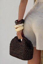 hand holding dark brown crochet clutch bag resin bangles linen shorts wall - brown - clutch bag