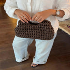 woman with both hands holding dark brown crochet clutch bag wearing white shirt jeans - brown - clutch bag