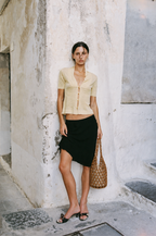 woman carrying tan wooden bead tote bag with yellow top and black skirt