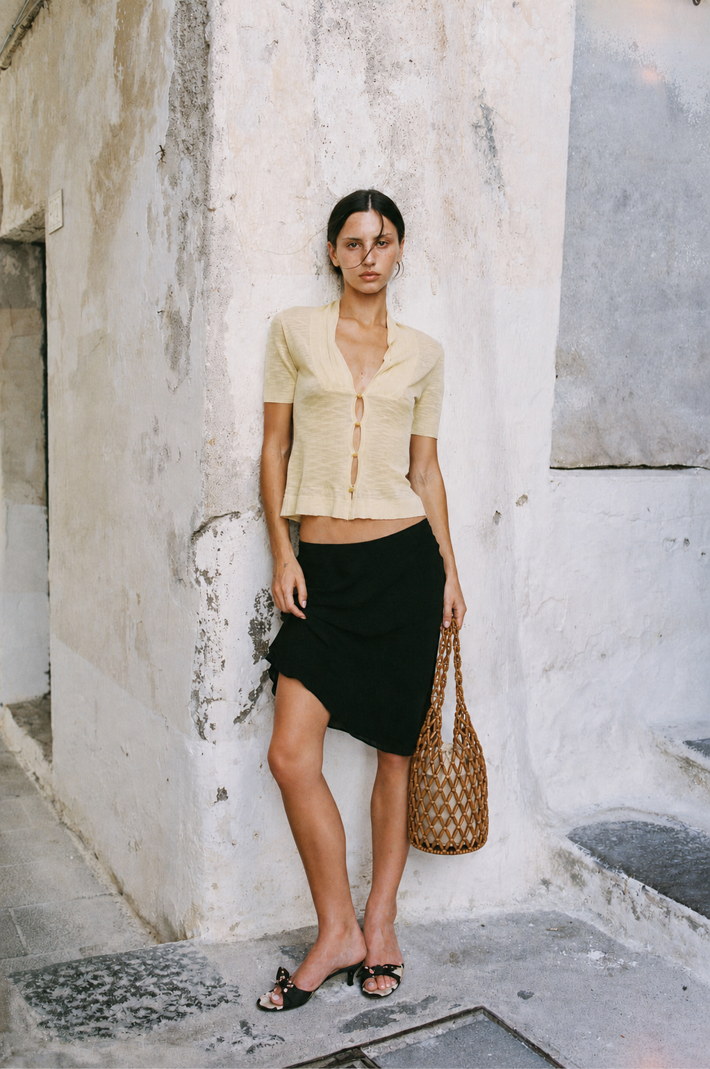 woman carrying tan wooden bead tote bag with yellow top and black skirt