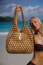 model holding up wooden bead tote bag on beach turquoise sea natural tan - tan - tote bag