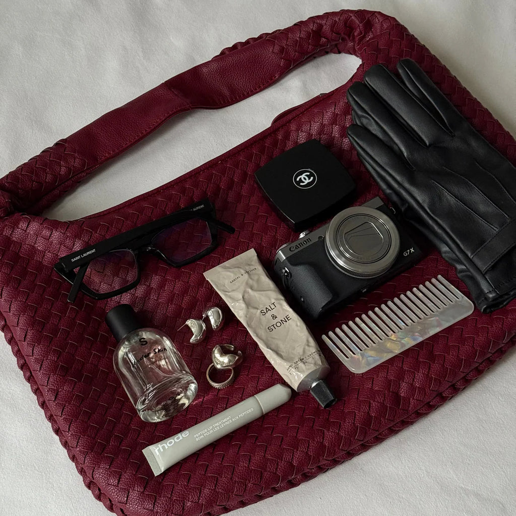 burgundy woven hobo shoulder bag flat lay with everyday essentials